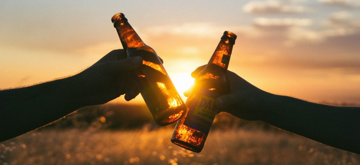 dva ľudia si štrngajú pivovými fľašami pri západe slnka