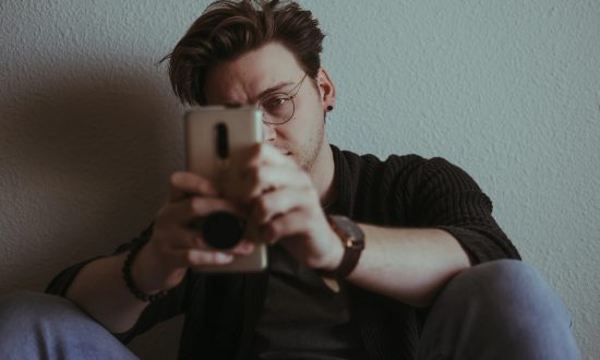 Sediaci smutný mladý muž, ktorý sa pozerá do mobilu