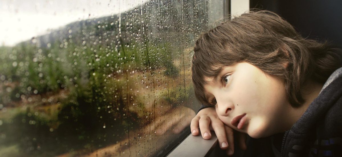 Smutný chlapec sa díva z okna.