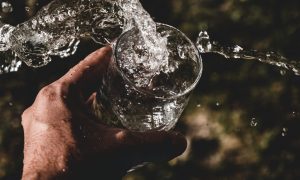 Ruka drží pohár s vodou – ochutnal by si vodu starú miliardy rokov?