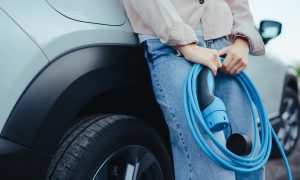 Žena drží nabíjací kábel z elektromobilu