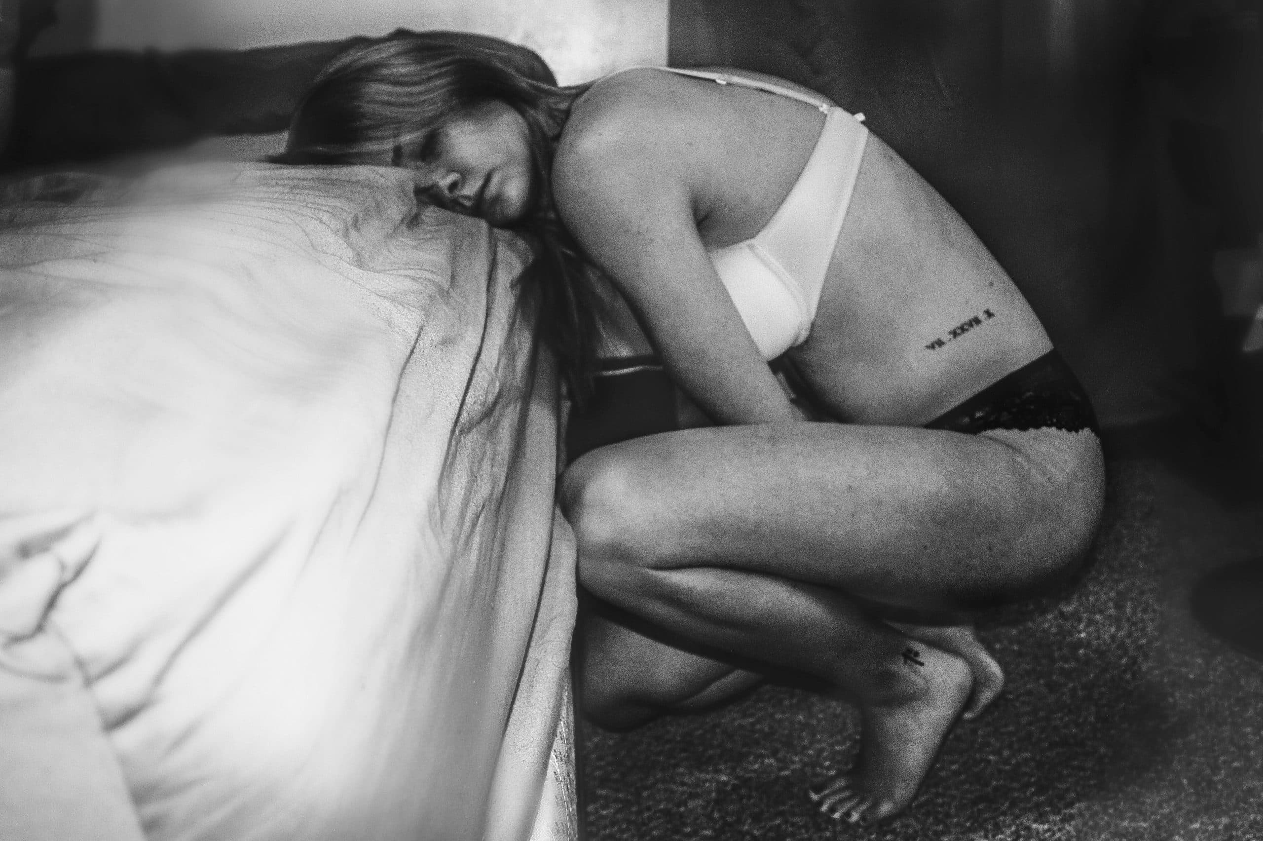 Čiernobiela fotka ženy krčiacej sa pri posteli 