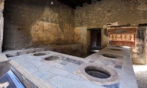 Zachované staroveké thermopolium v Pompejach s kamenným pultom a nádobami zapustenými do jeho povrchu.